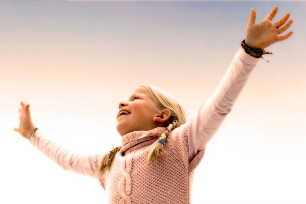 A joyful young girl with braided hair celebrates with arms raised outdoors. Captures happiness and freedom.