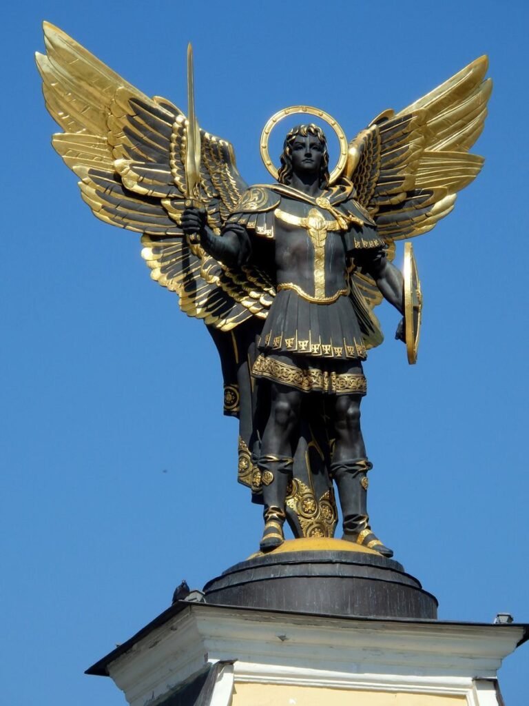 Bronze statue of Archangel Michael with sword and armor in Kyiv, Ukraine under clear blue sky.